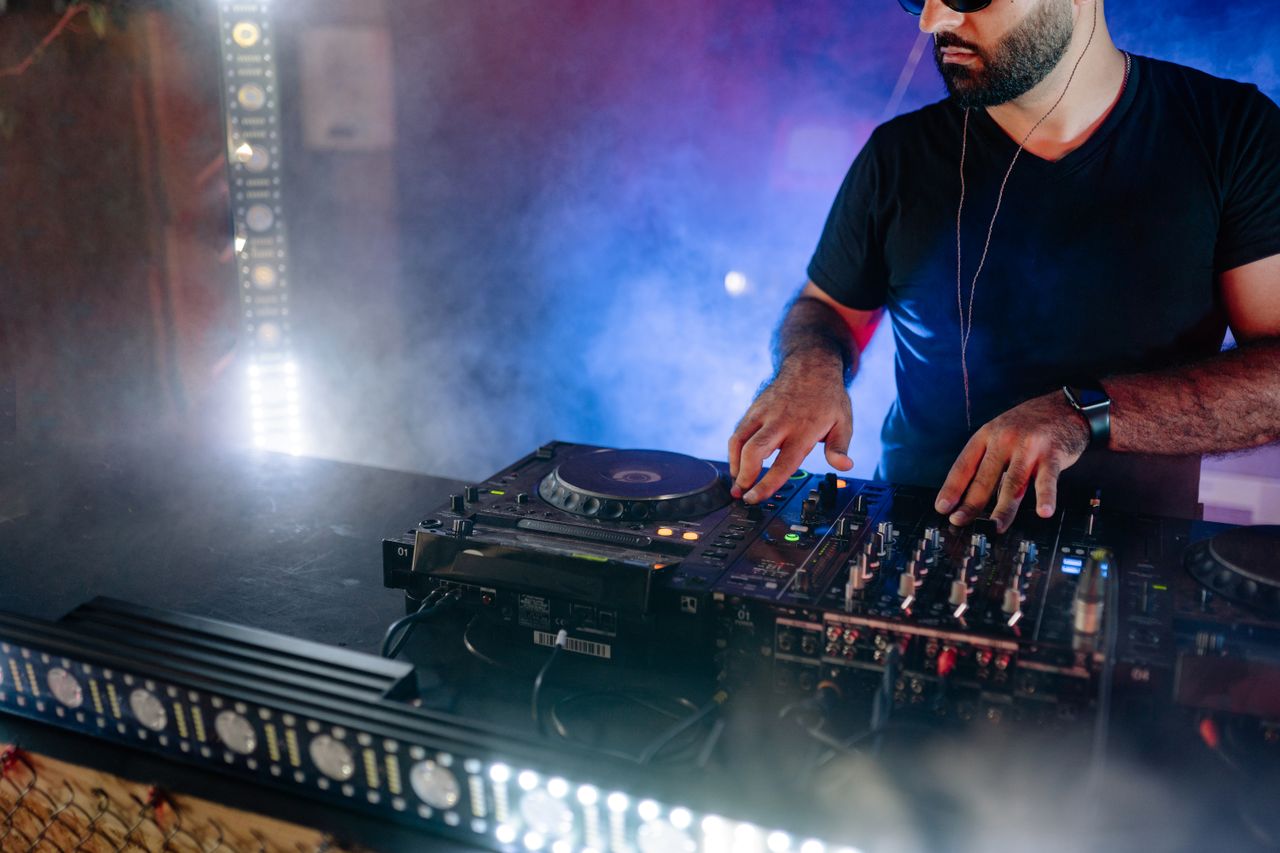 Services Energetic DJ performing live with mixing equipment in a colorful nightclub setting.